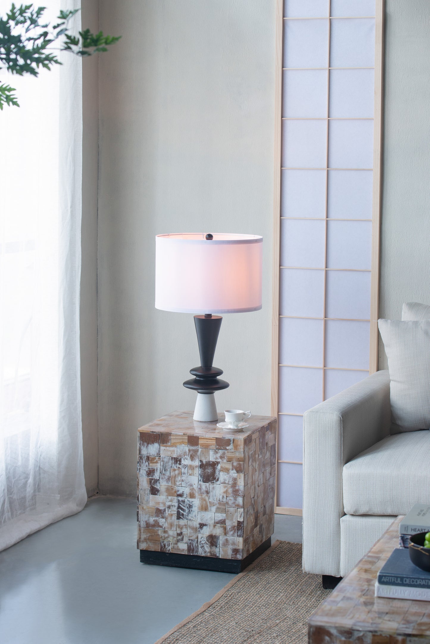 Table lamp in a living room on a mosaic-patterned side table, a sofa, and a plant.