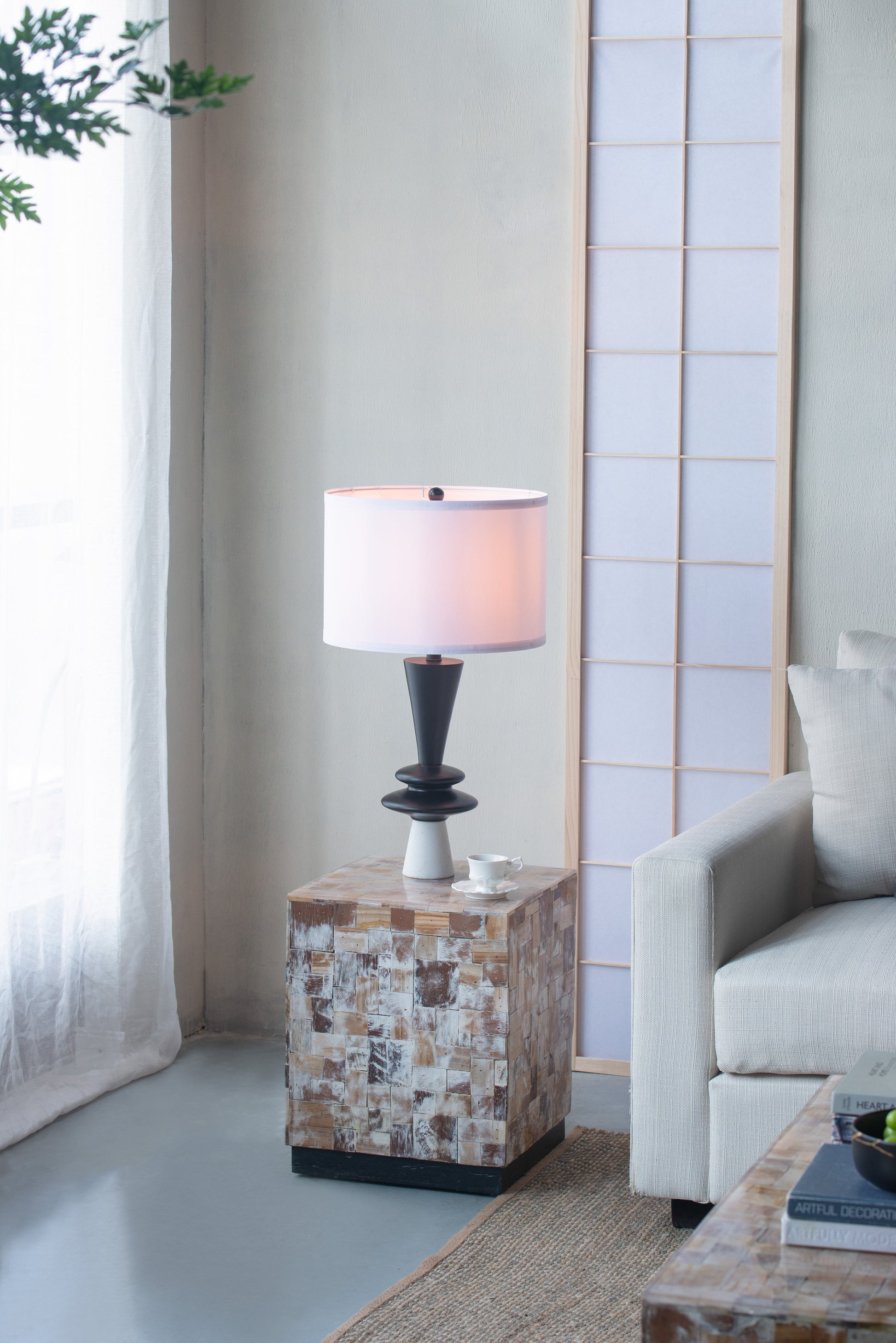 Table lamp in a living room on a mosaic-patterned side table, a sofa, and a plant.
