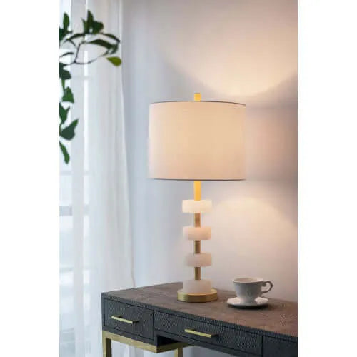 Table lamp on a wooden side table with a cup and saucer in a softly lit room.