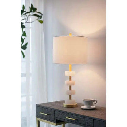 Table lamp on a wooden side table with a cup and saucer in a softly lit room.