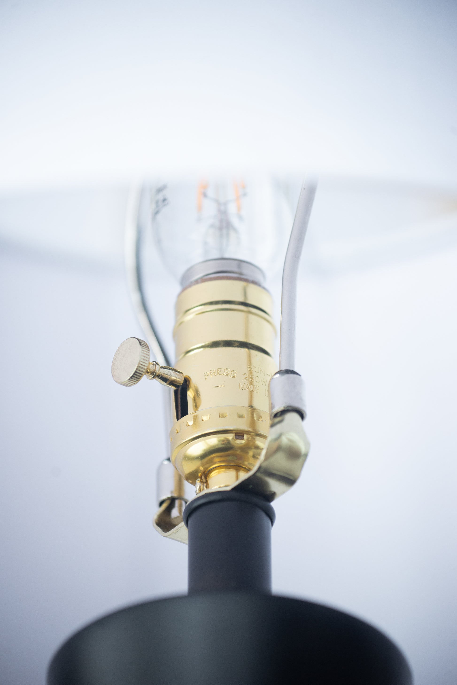Close-up of a lamp with a gold fitting and black base on a light gray background