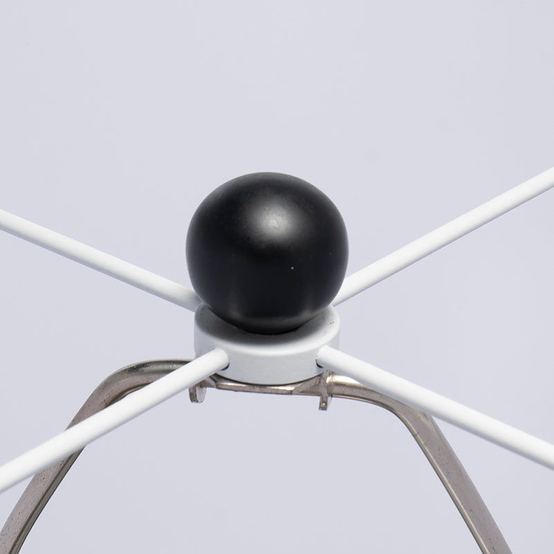 Close-up of a black spherical object on a white metal stand against a light gray background