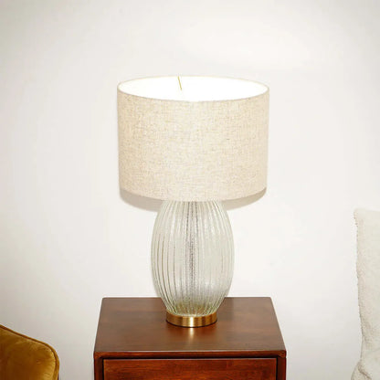 Table lamp with a textured glass base and beige fabric shade on a wooden side table.