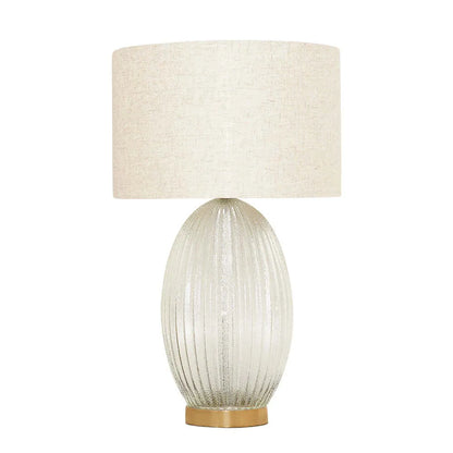 Table lamp with ribbed glass base and beige fabric shade on a white background