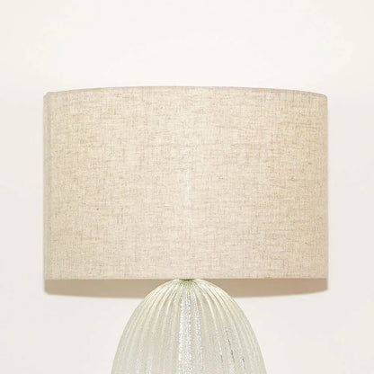 Table lamp with a beige fabric shade and ribbed glass base on a white background