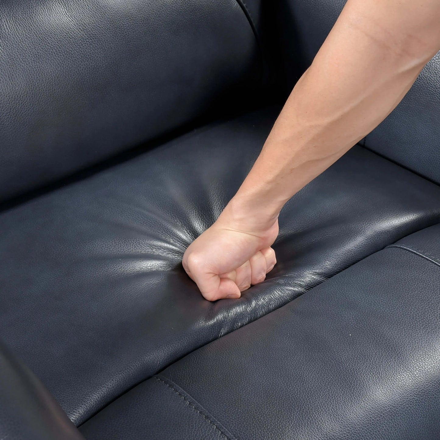 Hand pressing on a blue leather recliner chair seat cushion