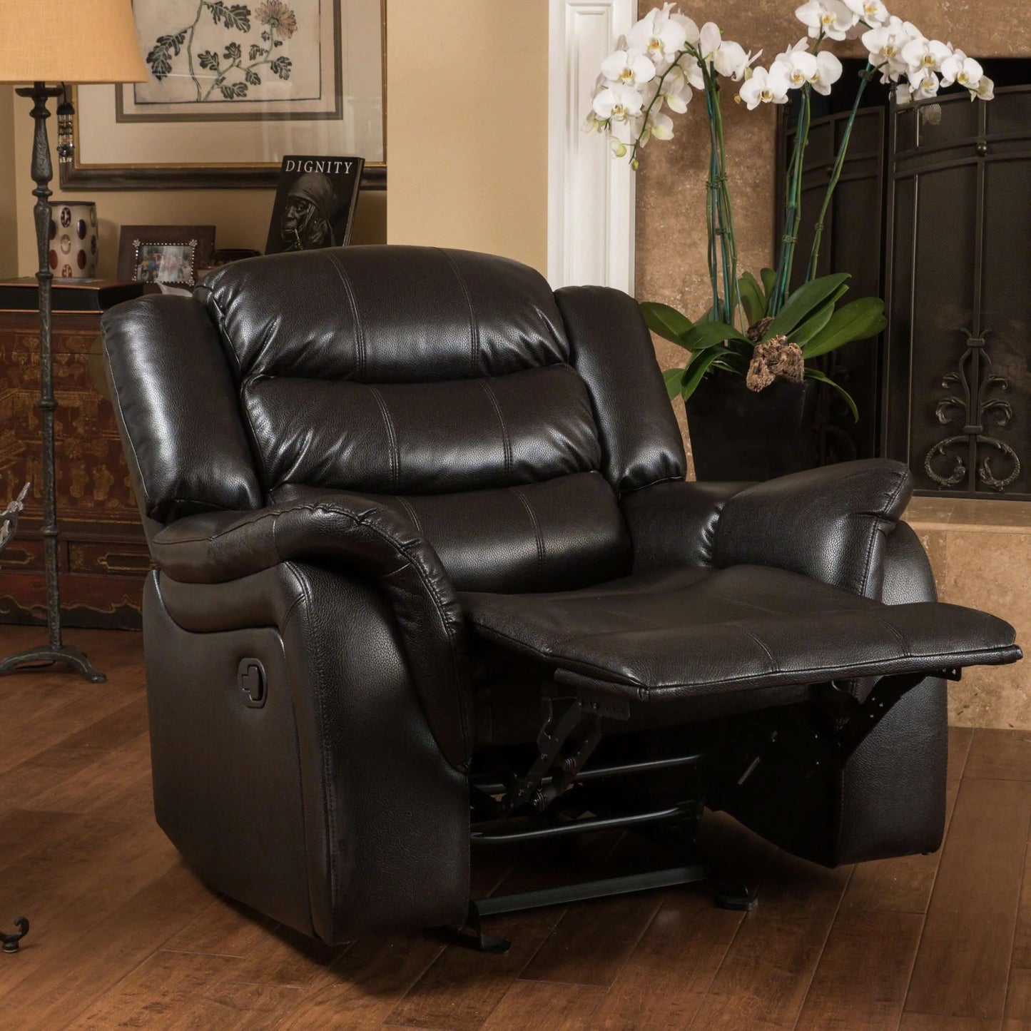 Black faux leather glider recliner chair in a reclining position in a living room setting with a lamp and decor.