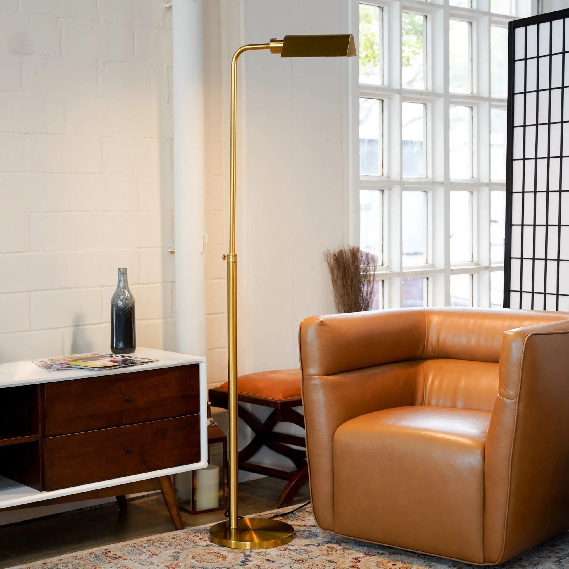 Modern living room with a brass floor lamp, brown leather armchair, and wooden side table.