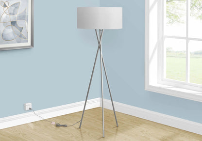 Tall floor lamp with a white shade in a room with light blue walls and a window.