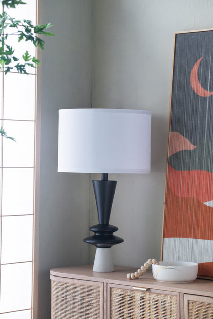 Table lamp with a white shade on a wooden cabinet against a wall with abstract art.