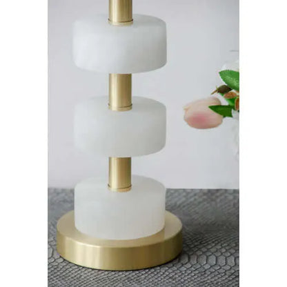 Decorative table lamp with white marble-like tiers and gold base on a textured surface.