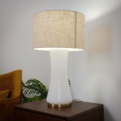 Table lamp with beige drum shade on a wooden surface against a neutral background