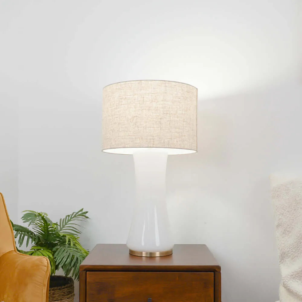 Table lamp with beige shade on a wooden side table against a white wall.