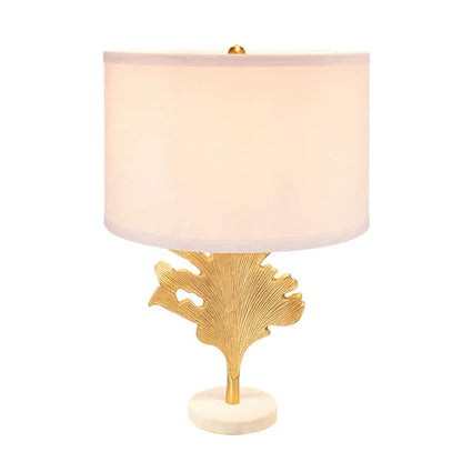Illuminated table lamp with gold leaf design and white shade on a white background