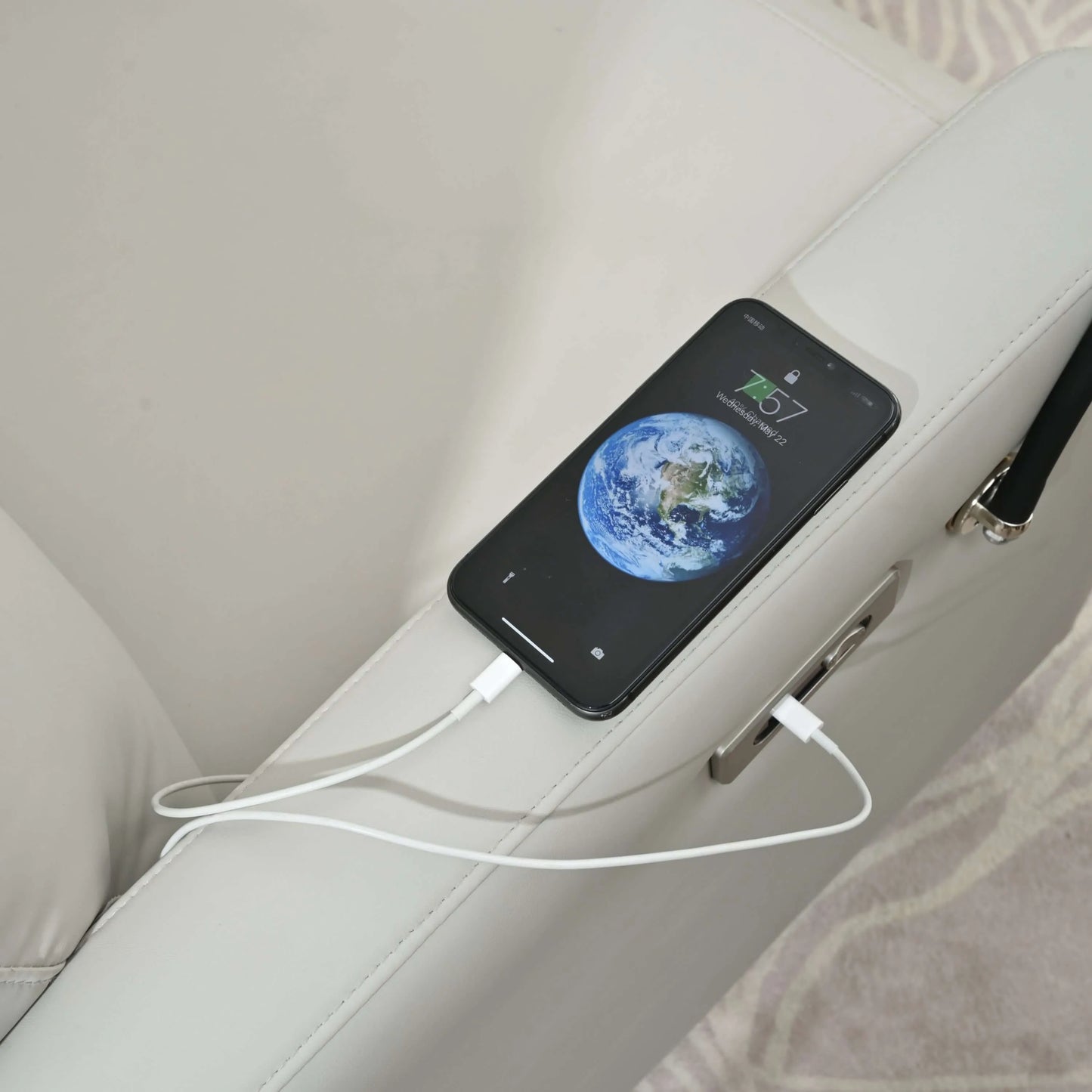 Smartphone charging on a light gray recliner armrest with a visible charging cable.