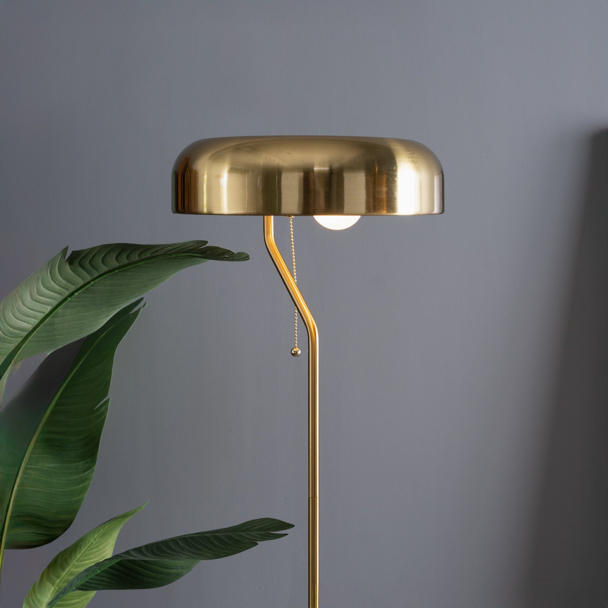 Gold floor lamp with a leafy plant against a gray wall
