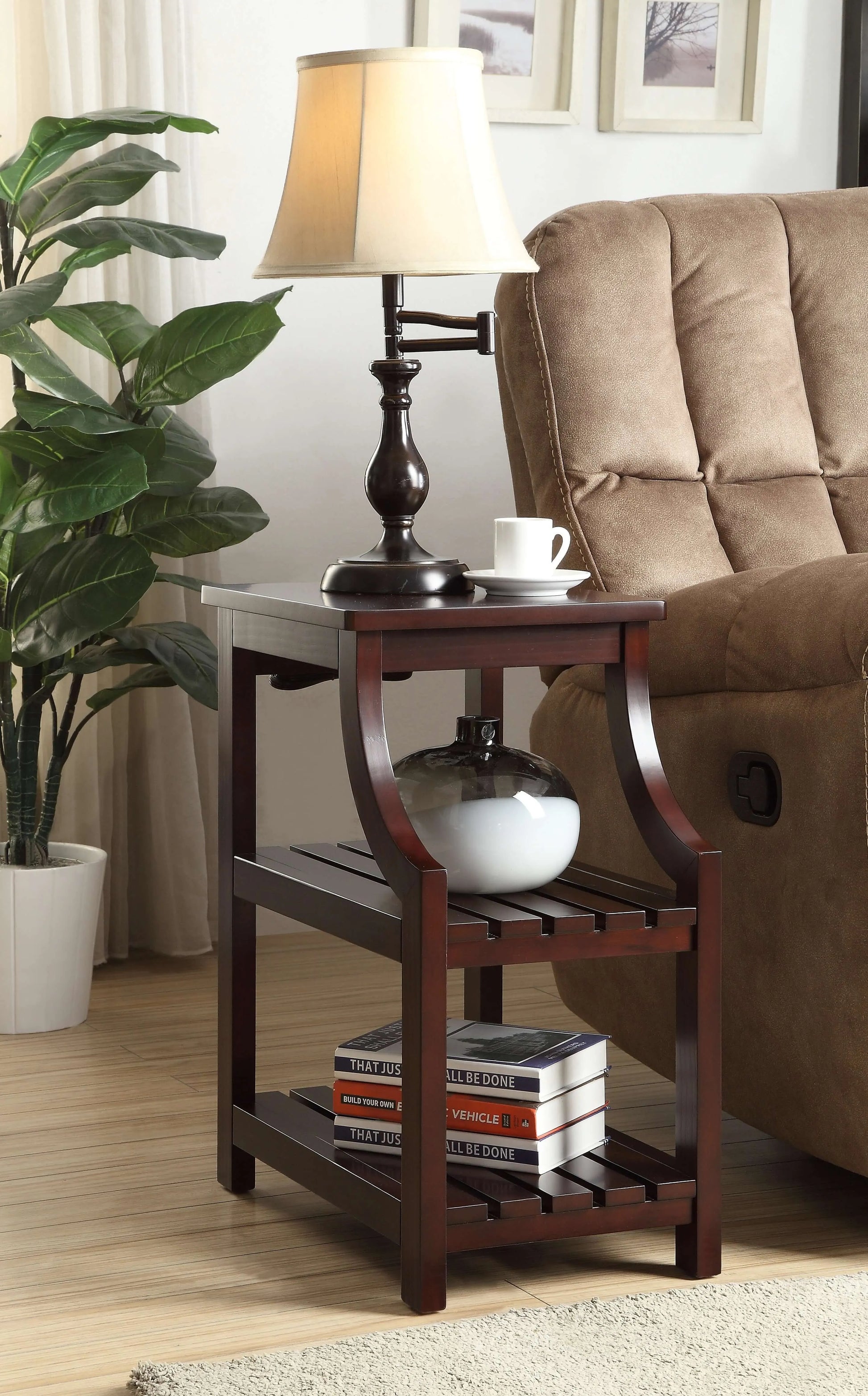 Wooden end table with lamp and books next to a brown sofa and plant