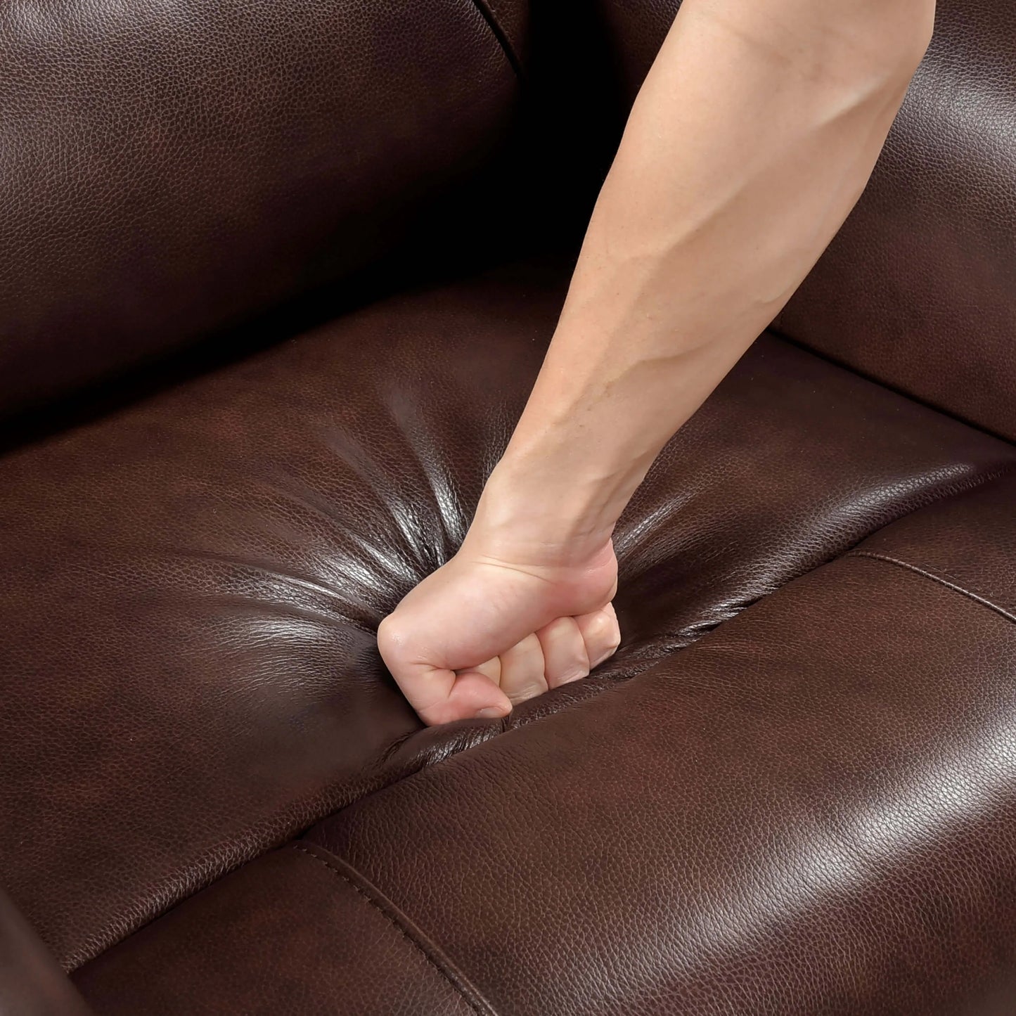 Person's fist on a brown leather recliner chair seat cushion.