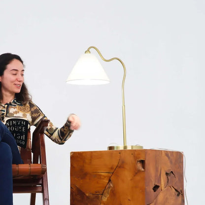Woman sitting next to a wooden table with a gold lamp on it