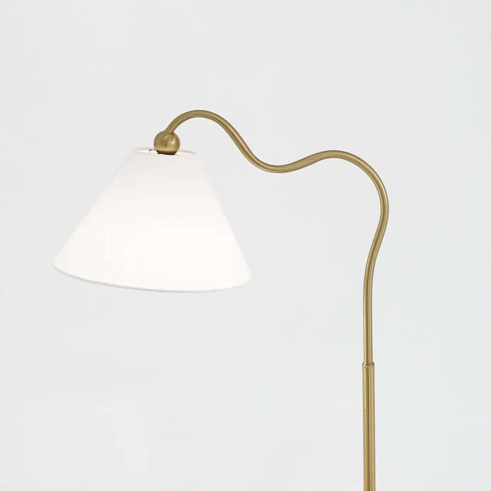 Close up of Floor lamp with white shade and brass curved arm on a light gray background
