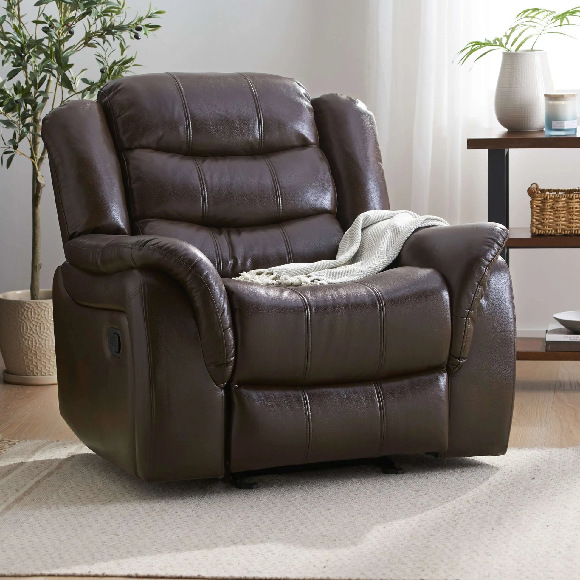Warm dark brown faux leather glider recliner chair in a living room setting with plants and a side table.