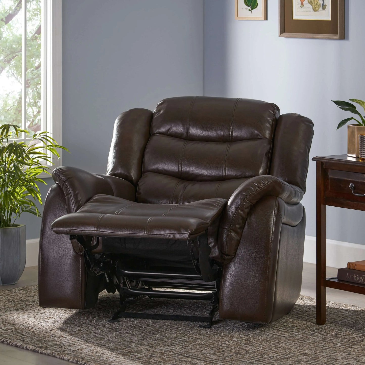 Warm dark brown faux leather glider recliner chair in a living room setting with plants and a side table.