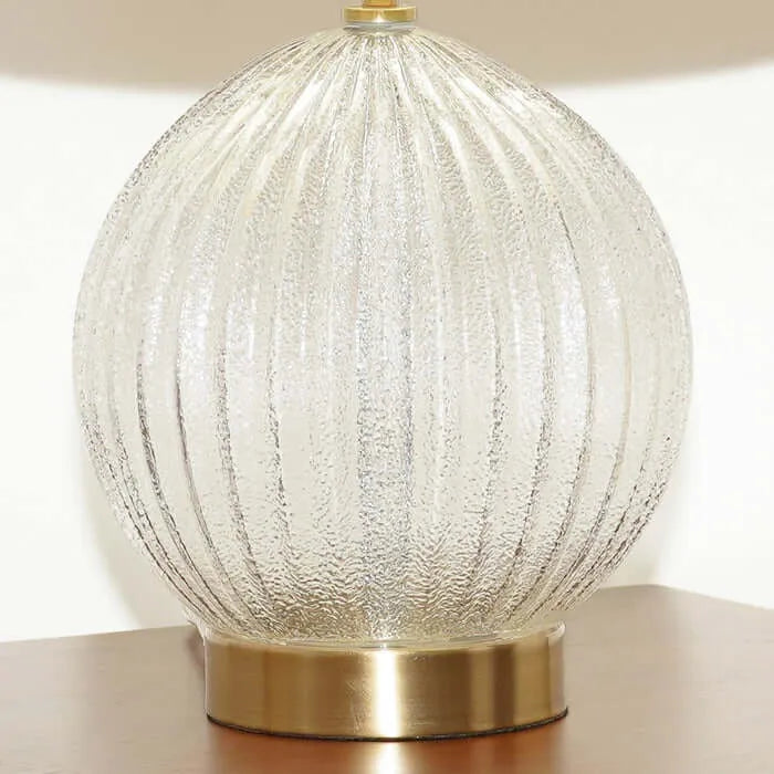 Decorative table lamp with textured ribbed glass body and brass base on a neutral background